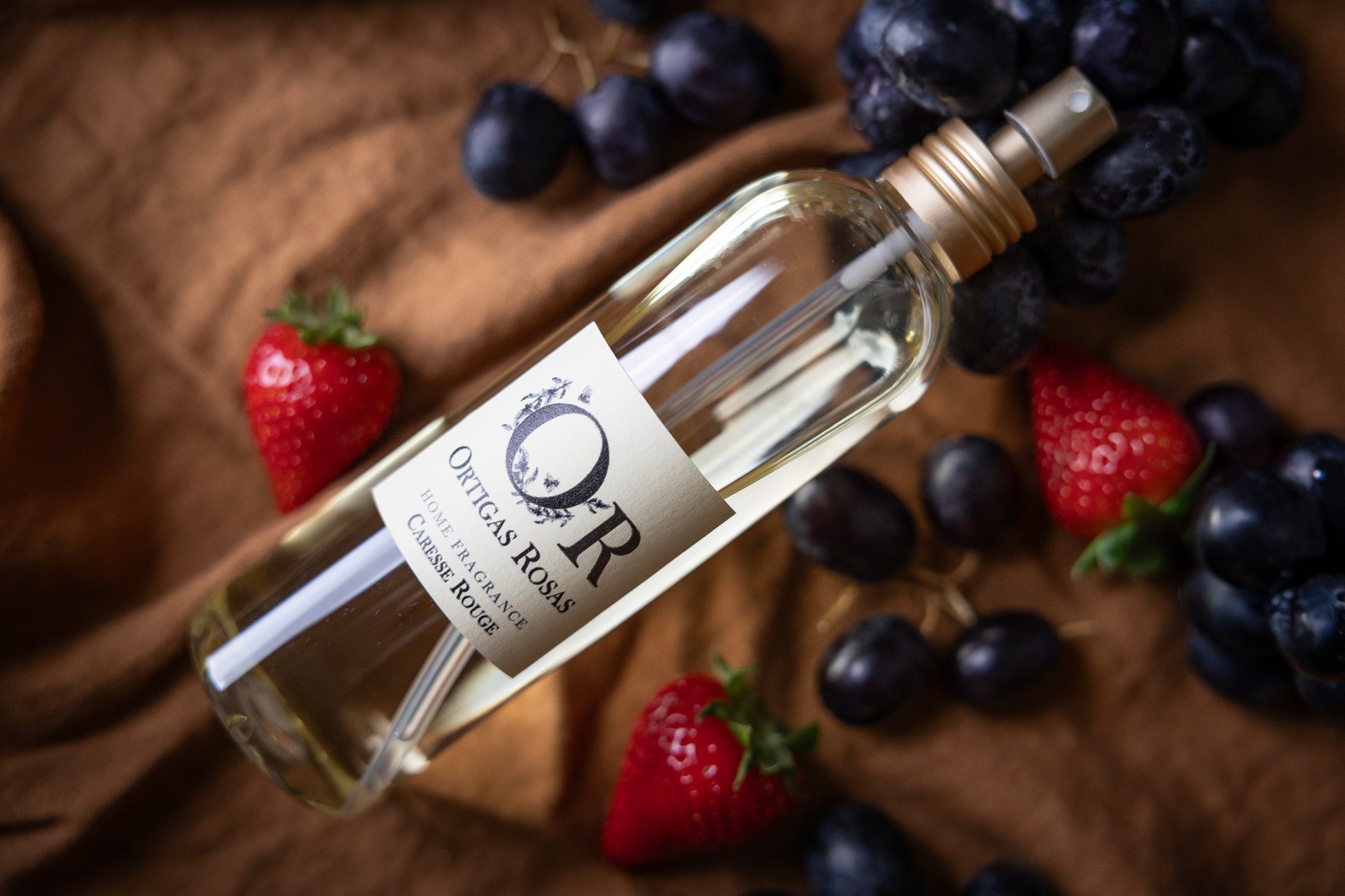 Caresse Rouge es una fragancia para hogar con notas de uva, fresa y cereza, se presenta en un envase transparente con tapón dorado y etiqueta color marfil