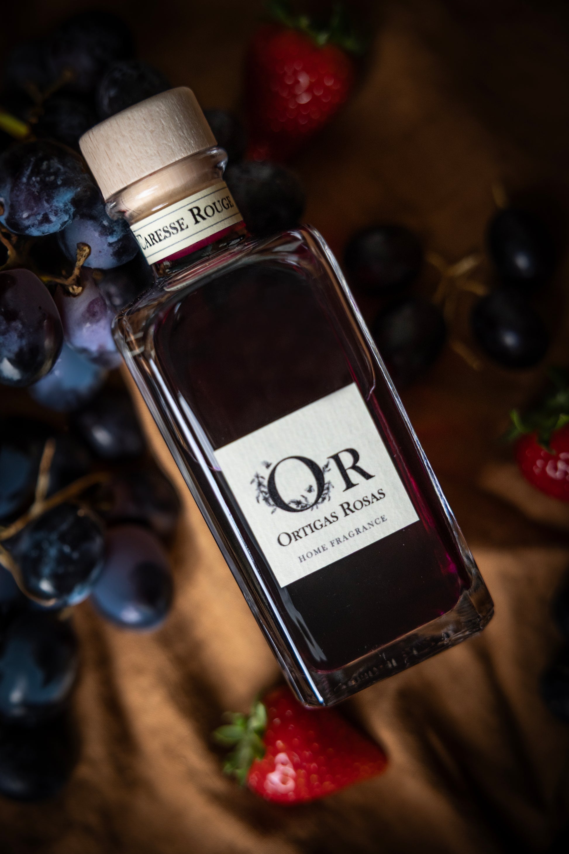 Caresse Rouge es una fragancia para hogar con notas de uva, fresa y cereza, se presenta en un envase transparente con tapón dorado y etiqueta color marfil