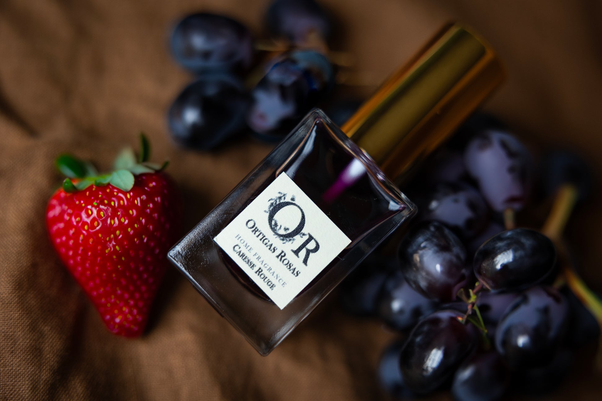 Caresse Rouge es una fragancia para hogar con notas de uva, fresa y cereza, se presenta en un envase transparente con tapón dorado y etiqueta color marfil