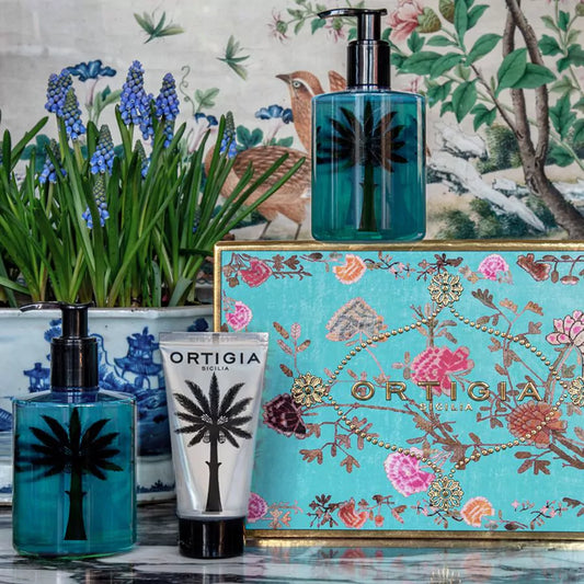 Frasco y estuche del perfume Ortigia Sicilia Florio con diseño de palmera sobre y flores con fondo color turquesa y caja con elementos dorados