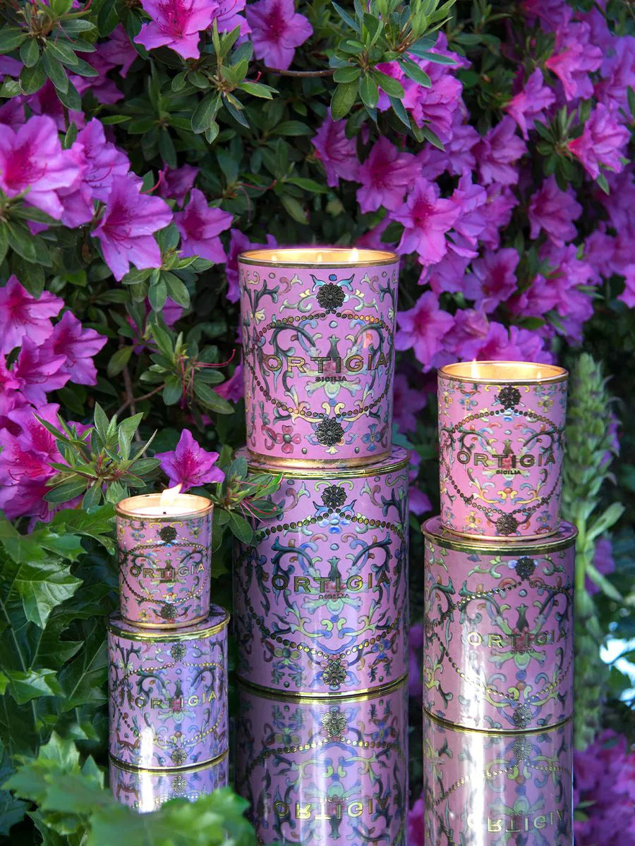 Decorative cylindrical Aragona containers candles with floral patterns stacked against a backdrop of pink flowers from Ortigia 