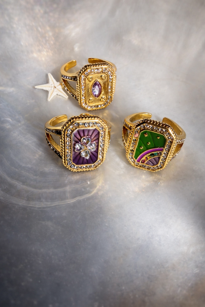 Three rectangular shaped gold rings with gemstones on a textured surface by ortigas rosas