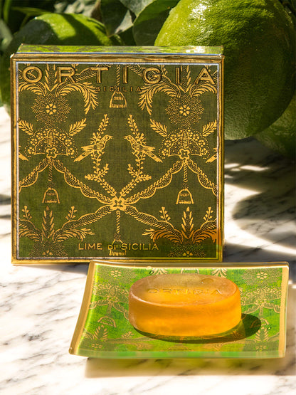 Bar of soap in a decorative green box with ornate design, placed on a marble surface with lime in the background.