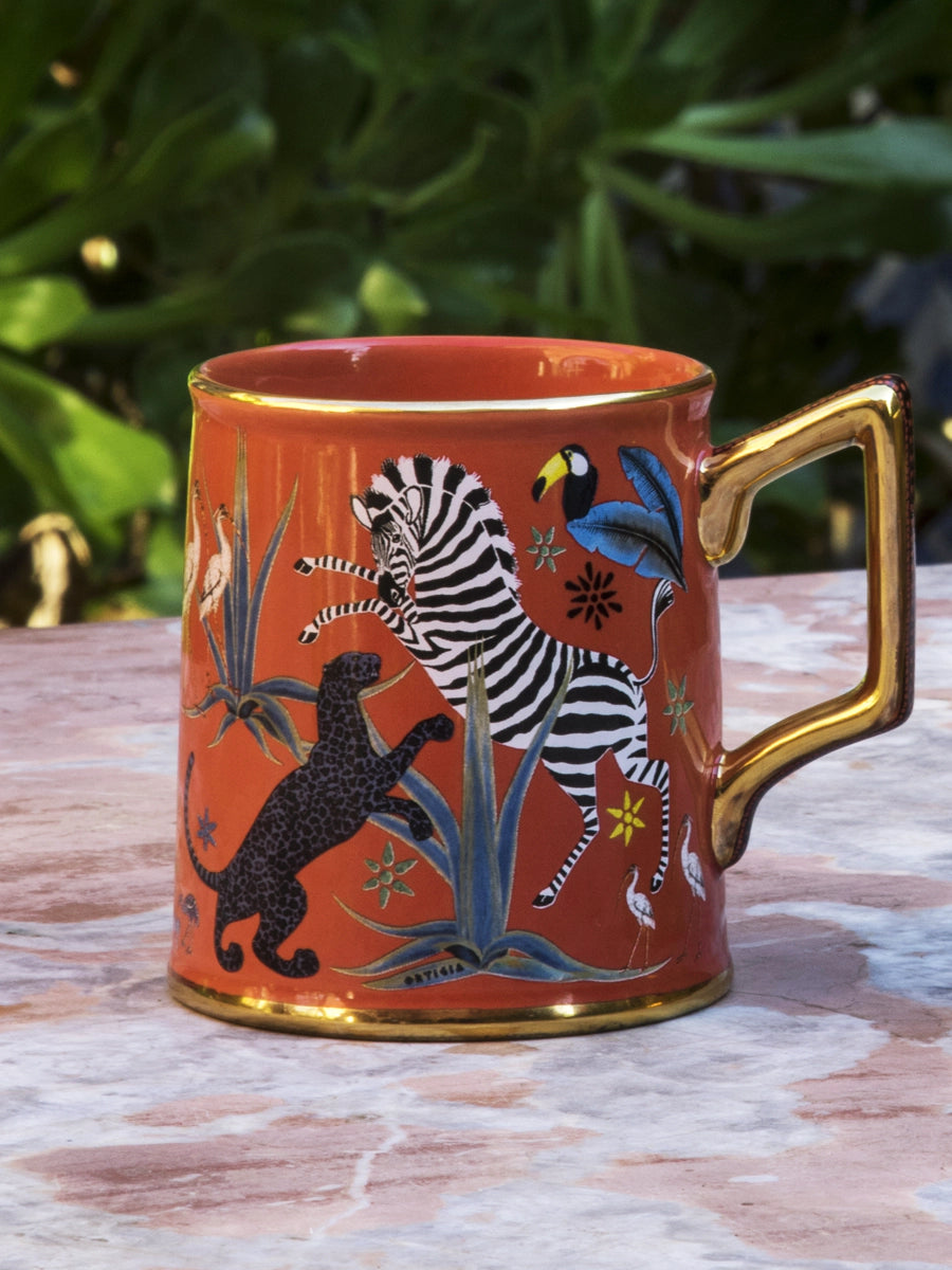 Taza roja con ilustraciones de animales y asa dorada, con la marca Ortigia.