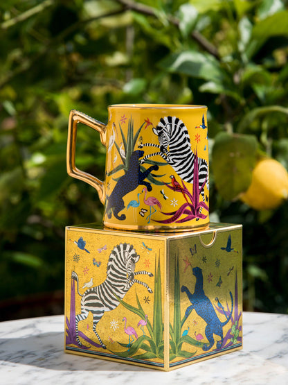 Taza amarilla con ilustraciones de animales y asa dorada, con la marca Ortigia y caja cuadrada decorada.