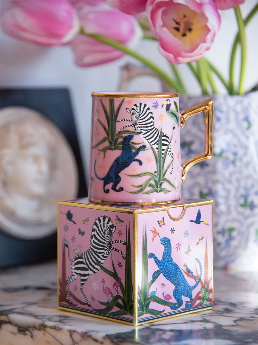 Taza color rosa con ilustraciones de animales y asa dorada, con la marca Ortigia y caja cuadrada decorada.