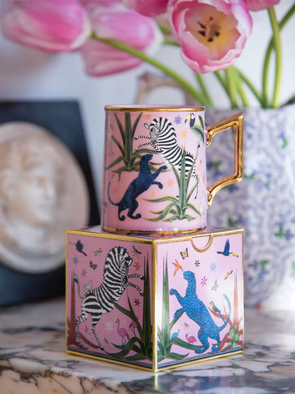 Taza color rosa con ilustraciones de animales y asa dorada, con la marca Ortigia y caja cuadrada decorada.